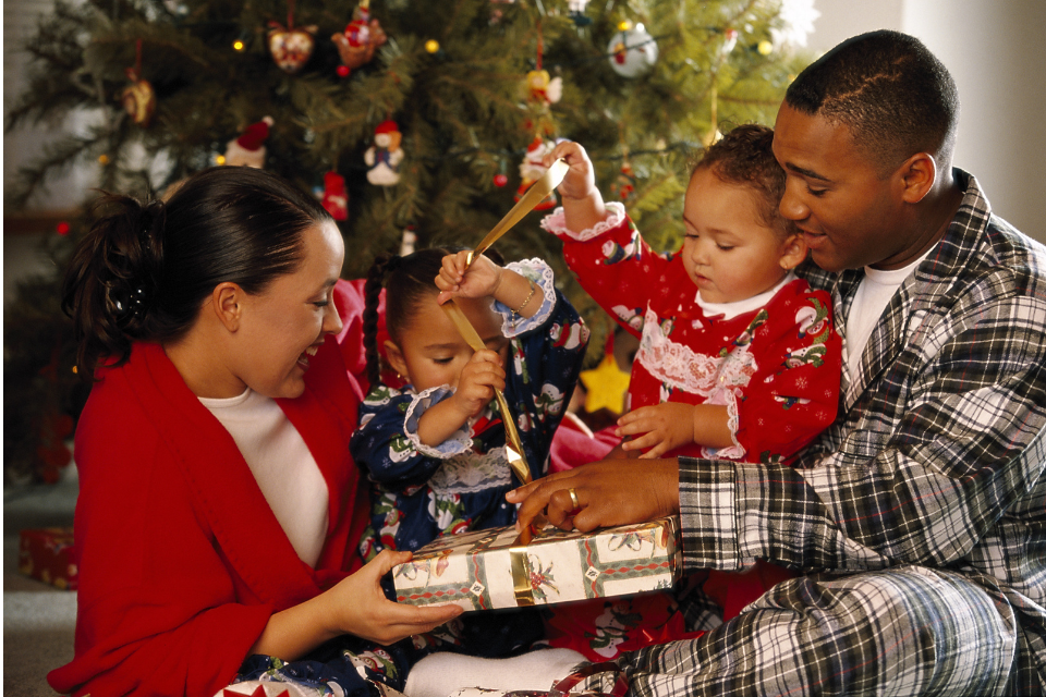 A happy family sitting by the Christmas tree, wearing festive pajamas and unwrapping gifts together in a warm holiday setting